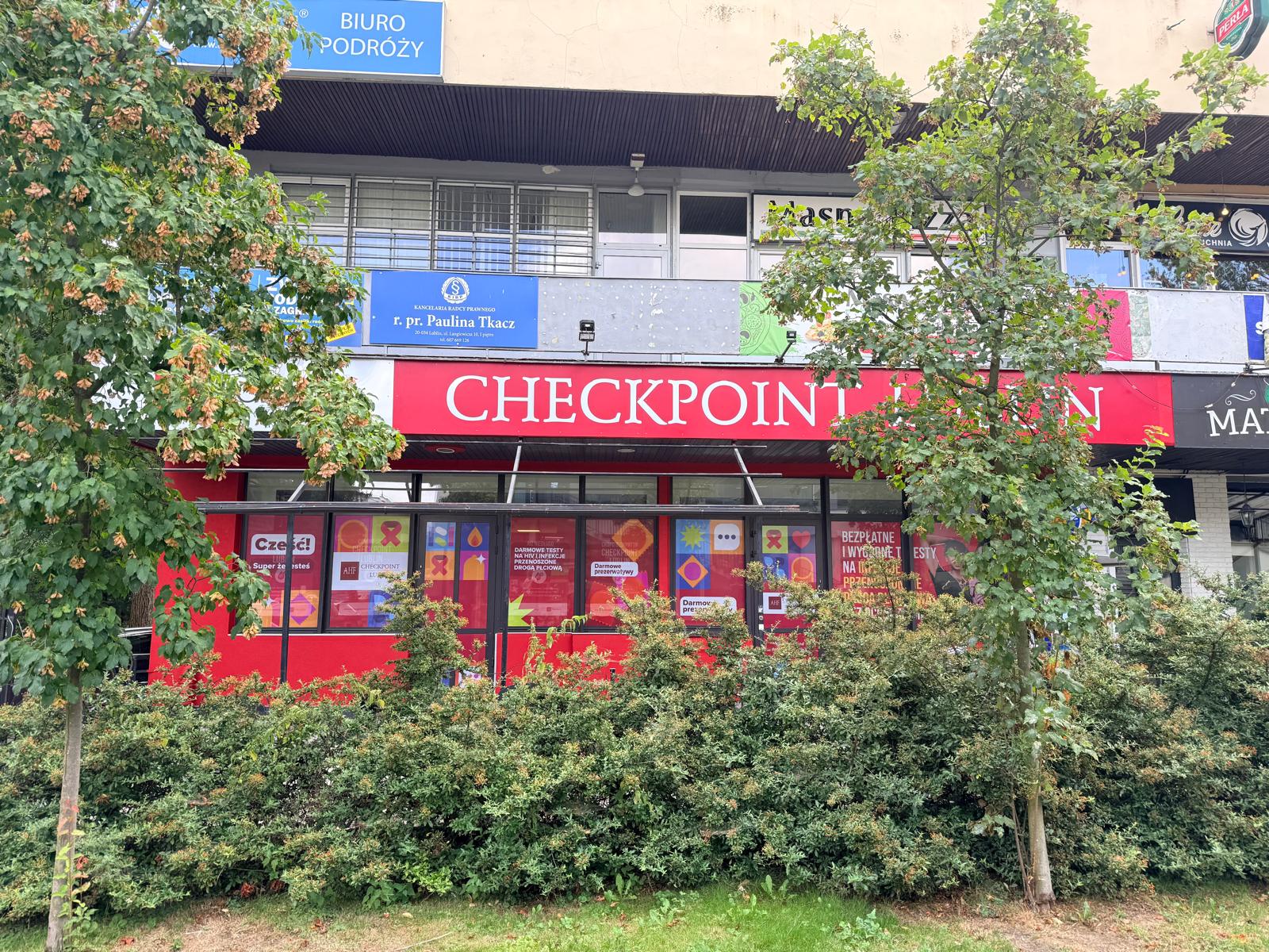 Exterior view of AHF Checkpoint Lublin, a community-based HIV and STI testing center in Lublin, Poland, with a red storefront and informational window displays